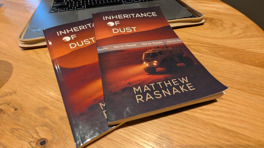 "Inheritance of Dust" proof prints lying on the front edge of a computer on a wooden table top.